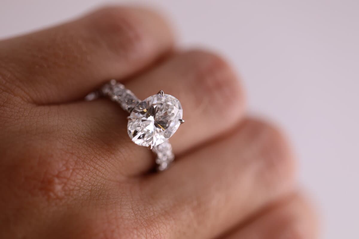 An oval diamond engagement ring with a diamond band, worn on a hand