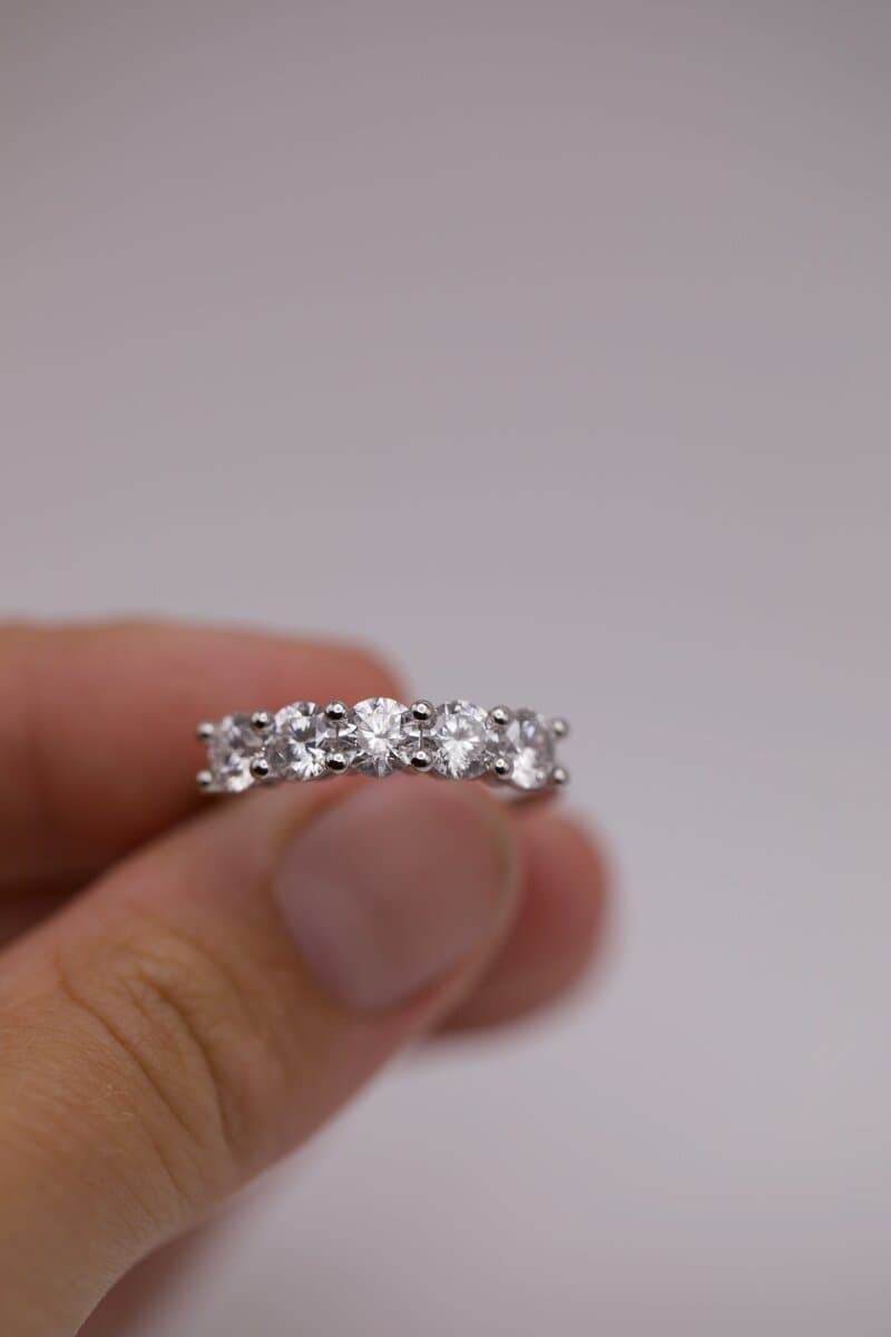 A five-stone band of round diamonds in shared prongs, held between two fingers
