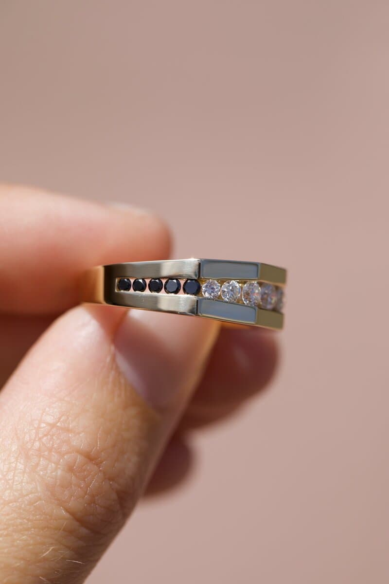 A yellow gold band with a row of channel-set dark and white stones, held between two fingers