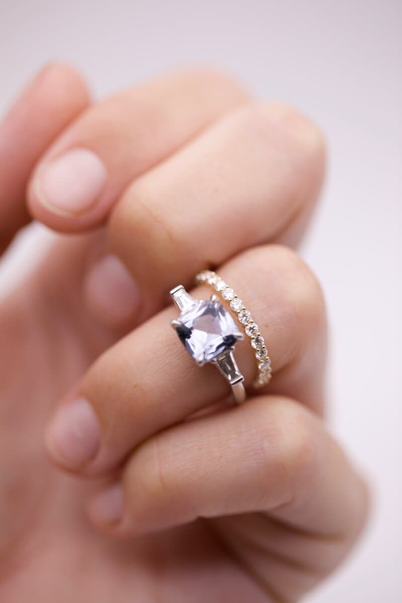 A hand wearing a pale blue cushion-cut stone ring with baguette sides and a thin diamond band