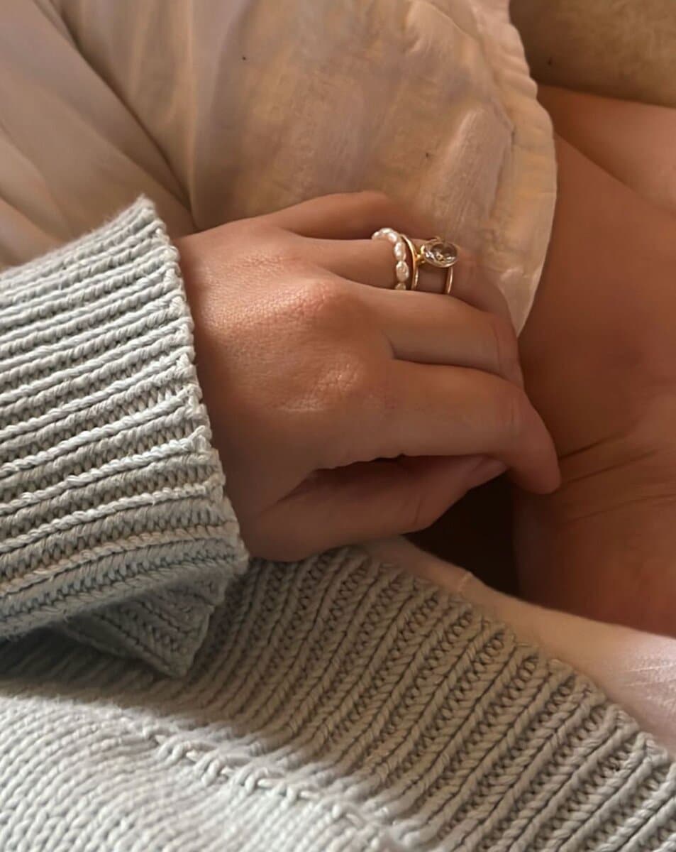 Two hands clasped over a knit sweater, one wearing a stack of three thin diamond bands