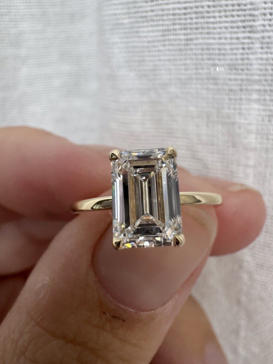 An emerald-cut diamond solitaire in yellow gold, held up against white linen