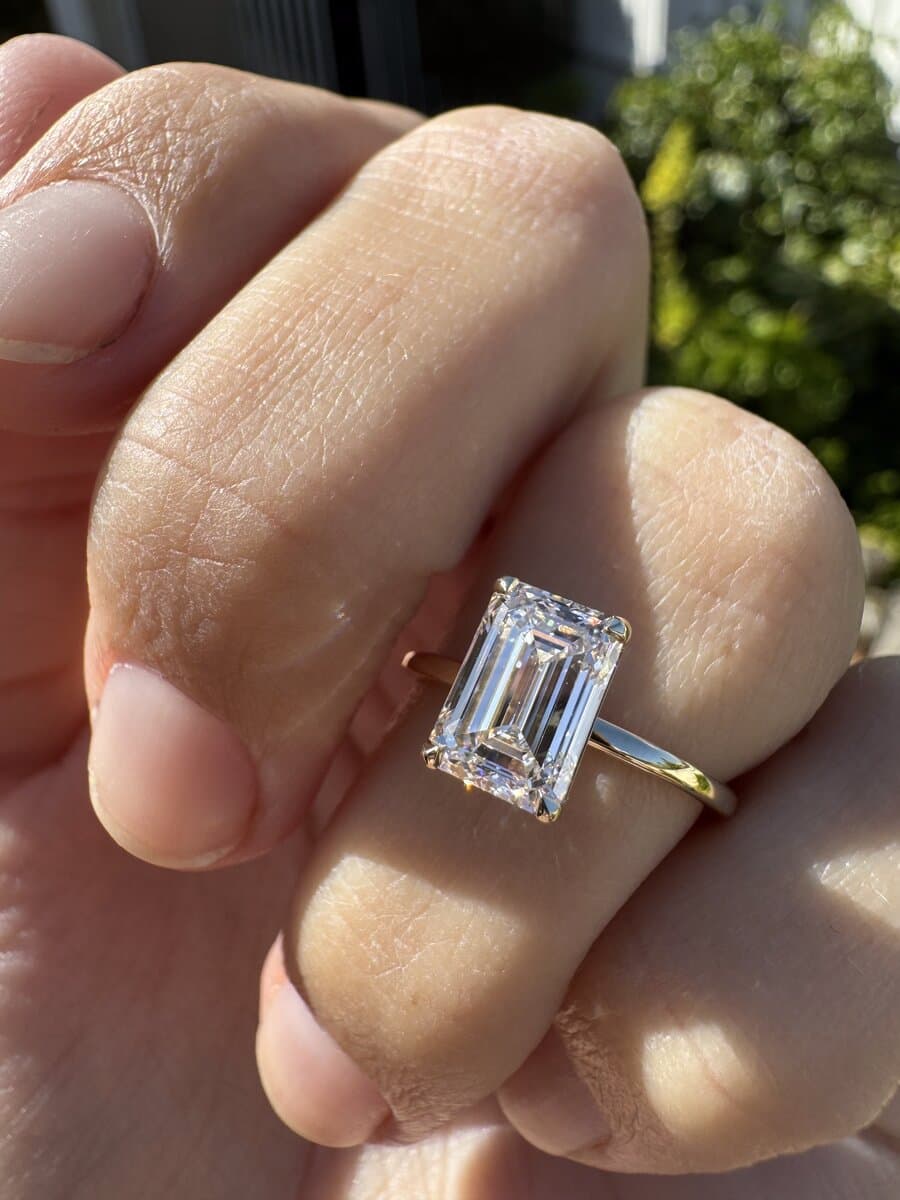 An emerald-cut diamond engagement ring in yellow gold, worn outdoors by a client of Sara Lundquist