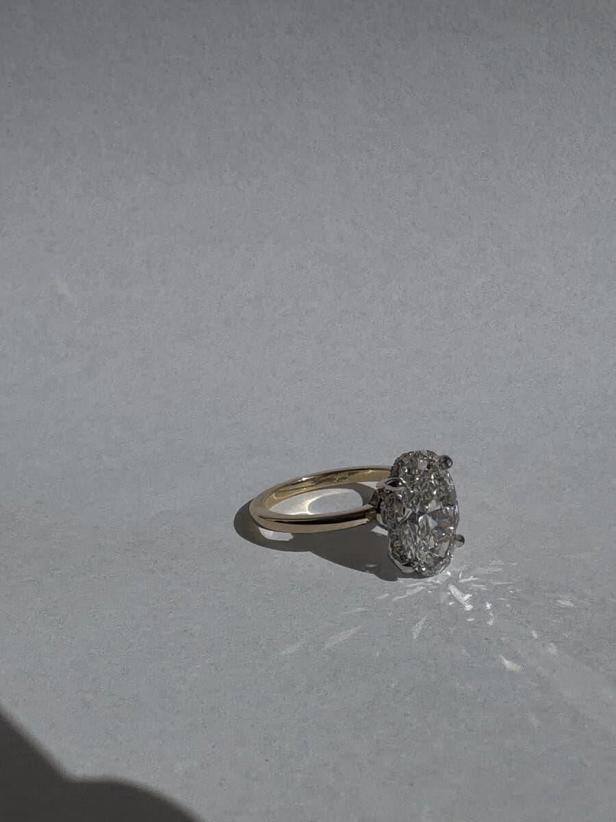 An oval diamond set in a slim yellow gold band, photographed from the side