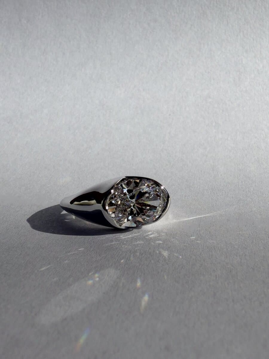 A round diamond in a white-metal bezel ring, photographed on a white surface