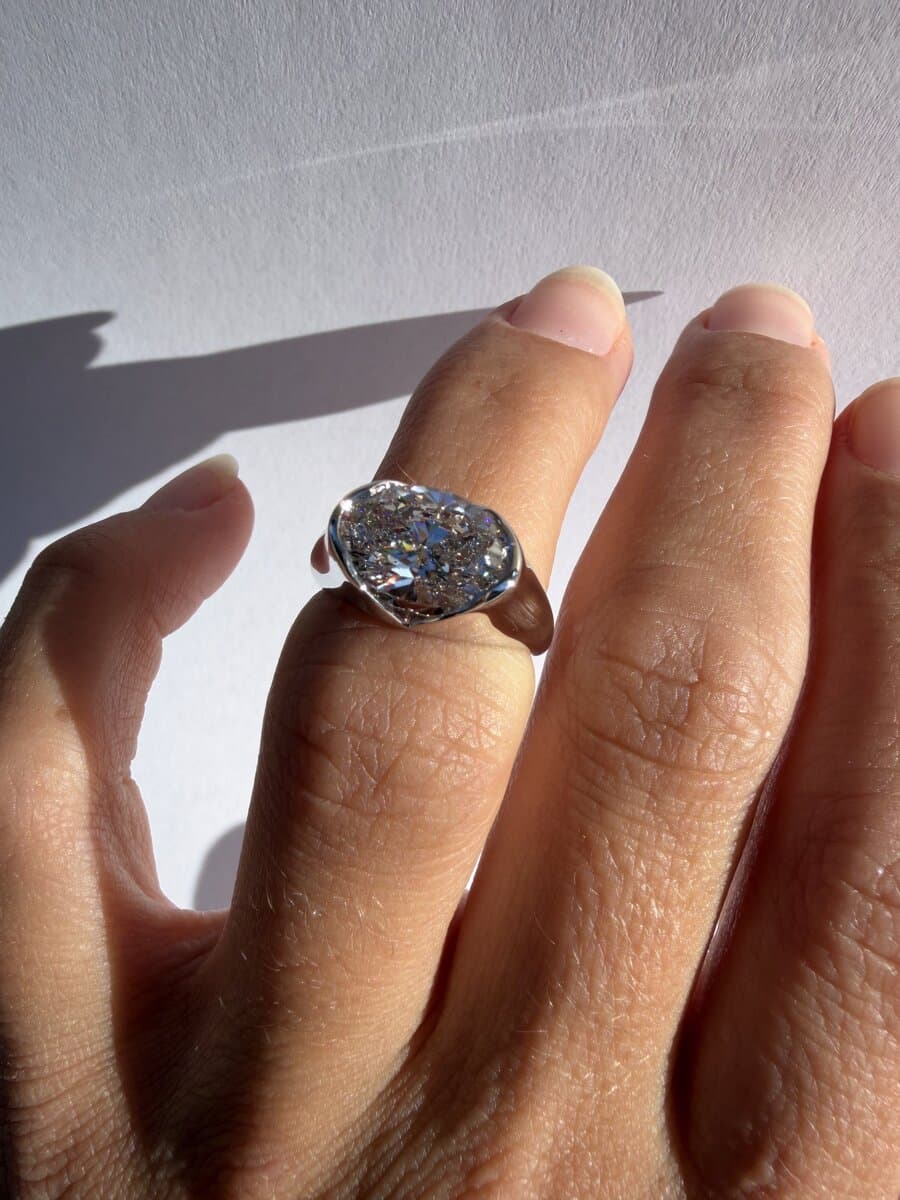 A hand wearing a white-metal signet-style ring with a marquise diamond set east-west