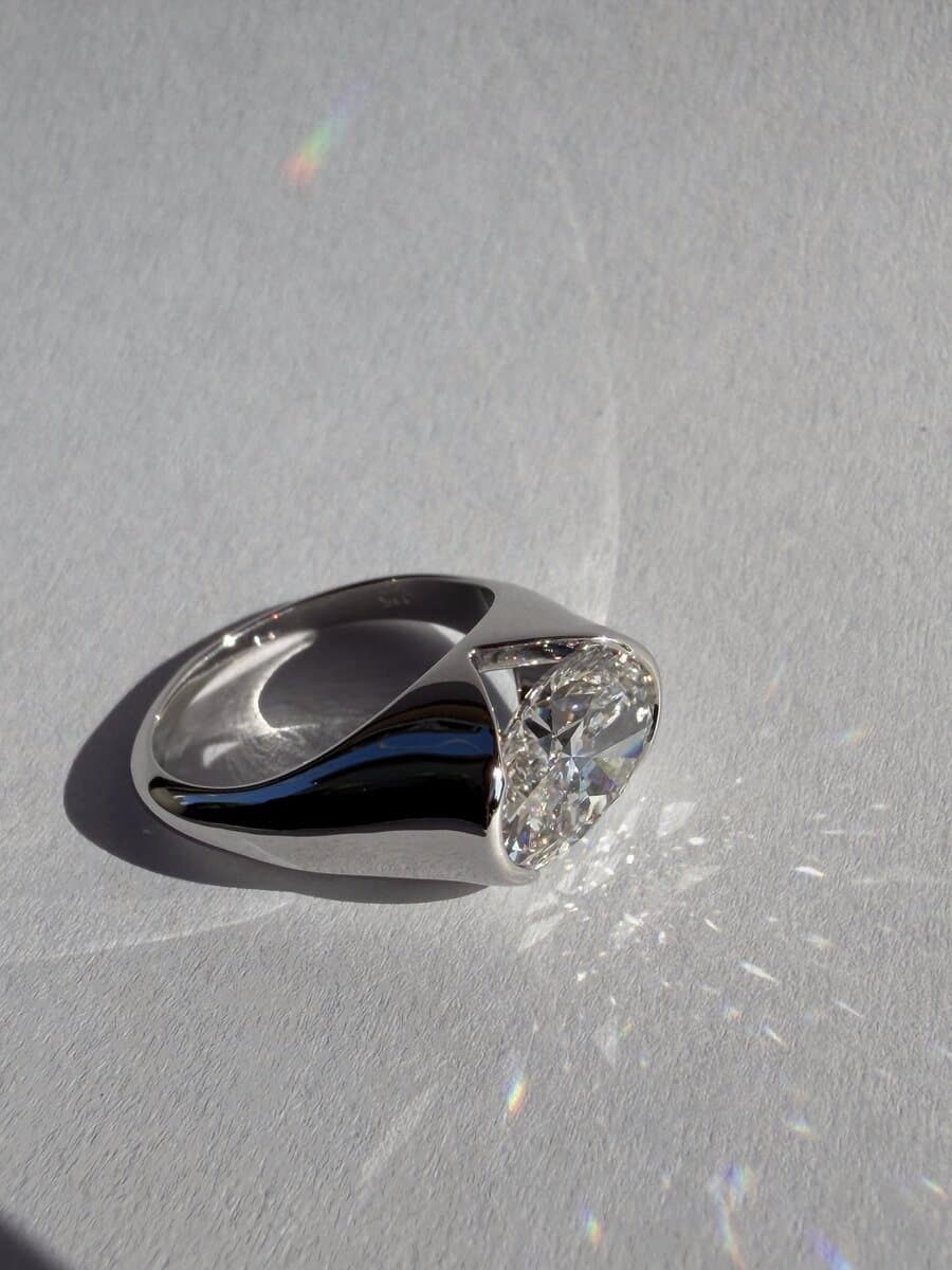 An oval diamond ring in yellow gold, photographed on a white surface