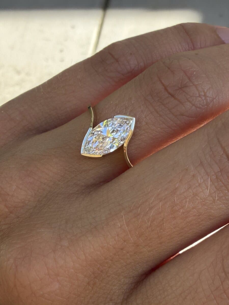 A hand wearing a marquise diamond in a yellow gold bezel bypass ring