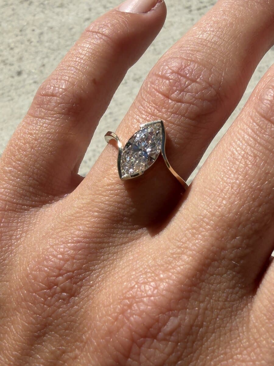 A marquise diamond in a yellow gold bezel bypass ring, worn on a hand