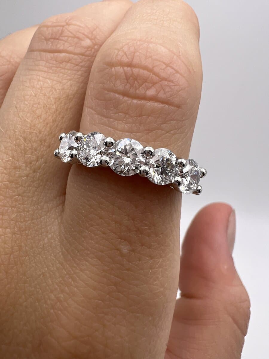 A hand wearing a five-stone band of round diamonds in shared prongs