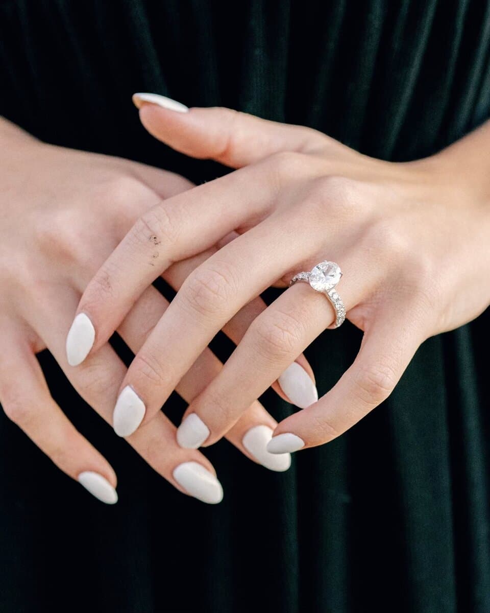 A client's hands resting on green velvet, wearing an oval diamond engagement ring by Sara Lundquist
