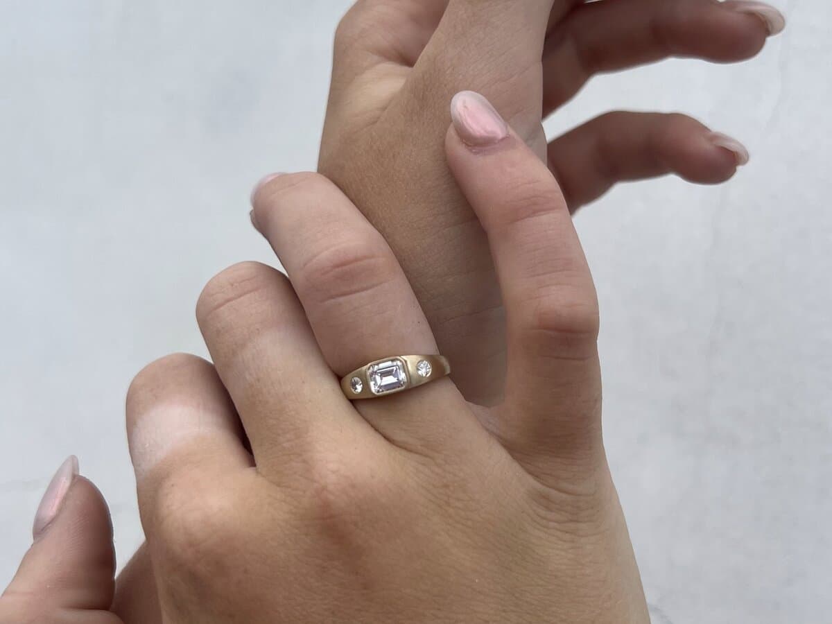 Two hands wearing a plain gold band, showing how a ring sits at the base of the finger