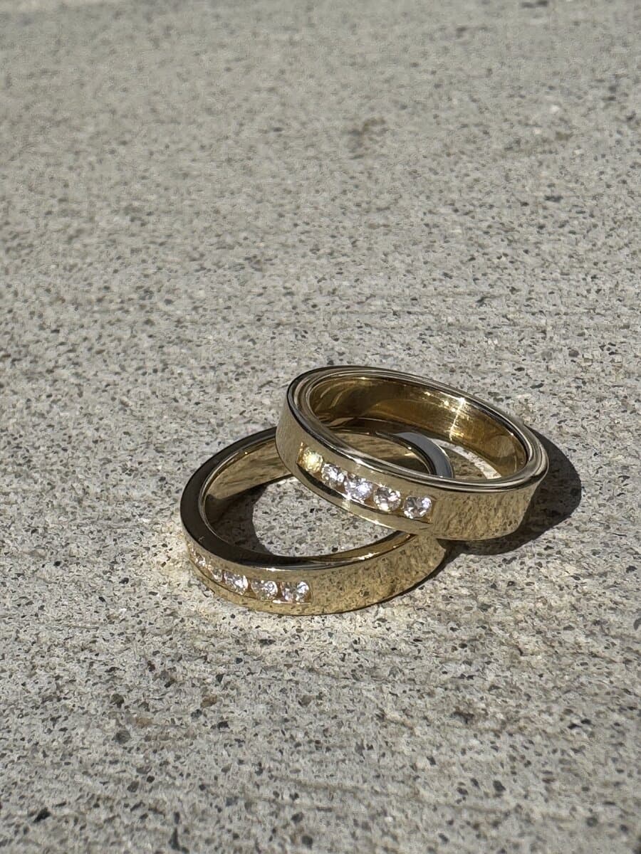 Two yellow gold bands with channel-set diamonds, stacked on a stone surface