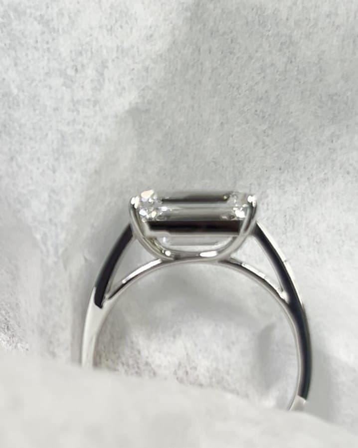 Side view of an emerald-cut diamond ring in white metal, showing the open shoulders under the stone