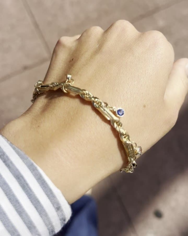 A textured yellow gold bracelet with small blue and red gemstone accents, worn on a wrist