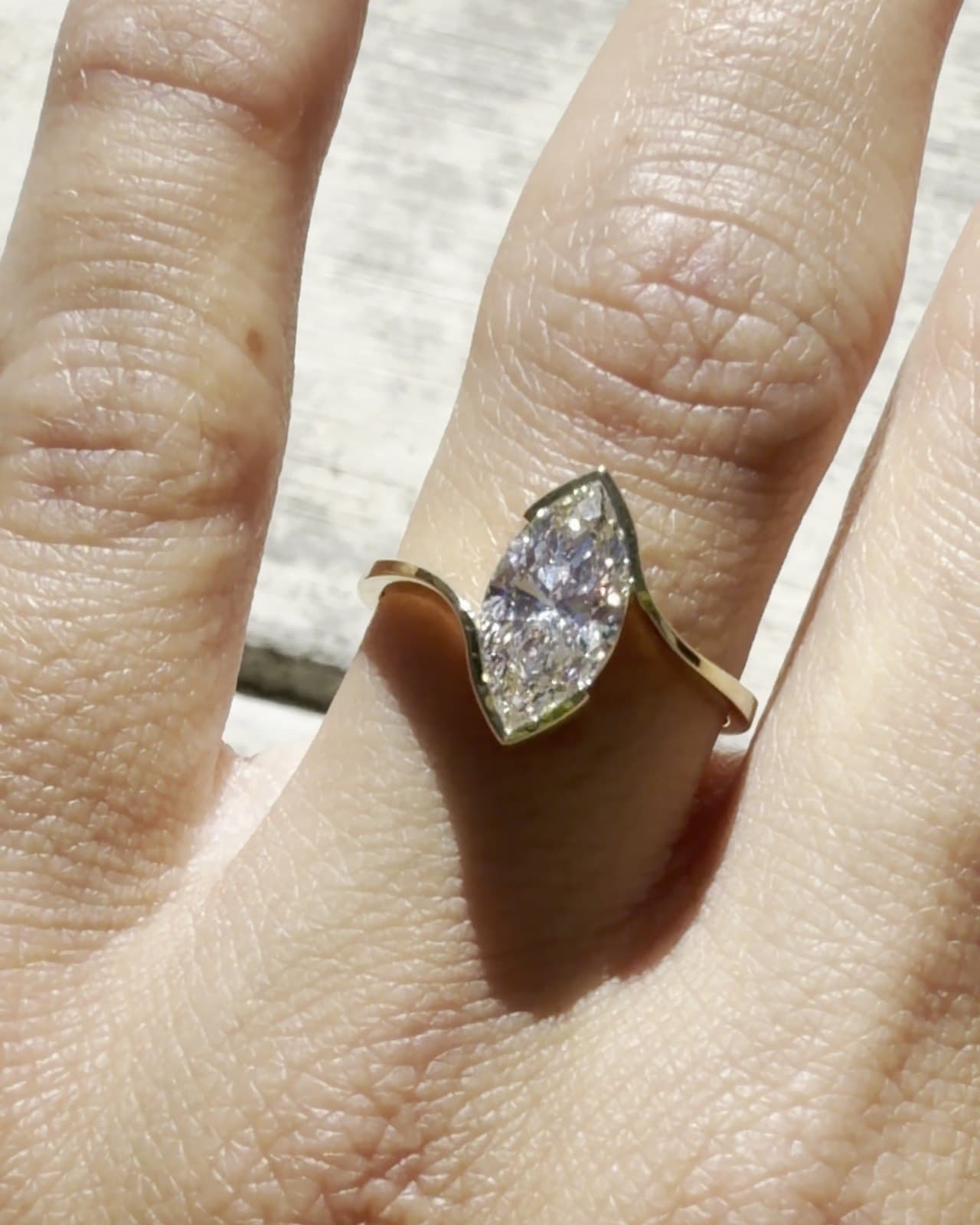 A marquise diamond set in a yellow gold bypass ring, worn on a hand