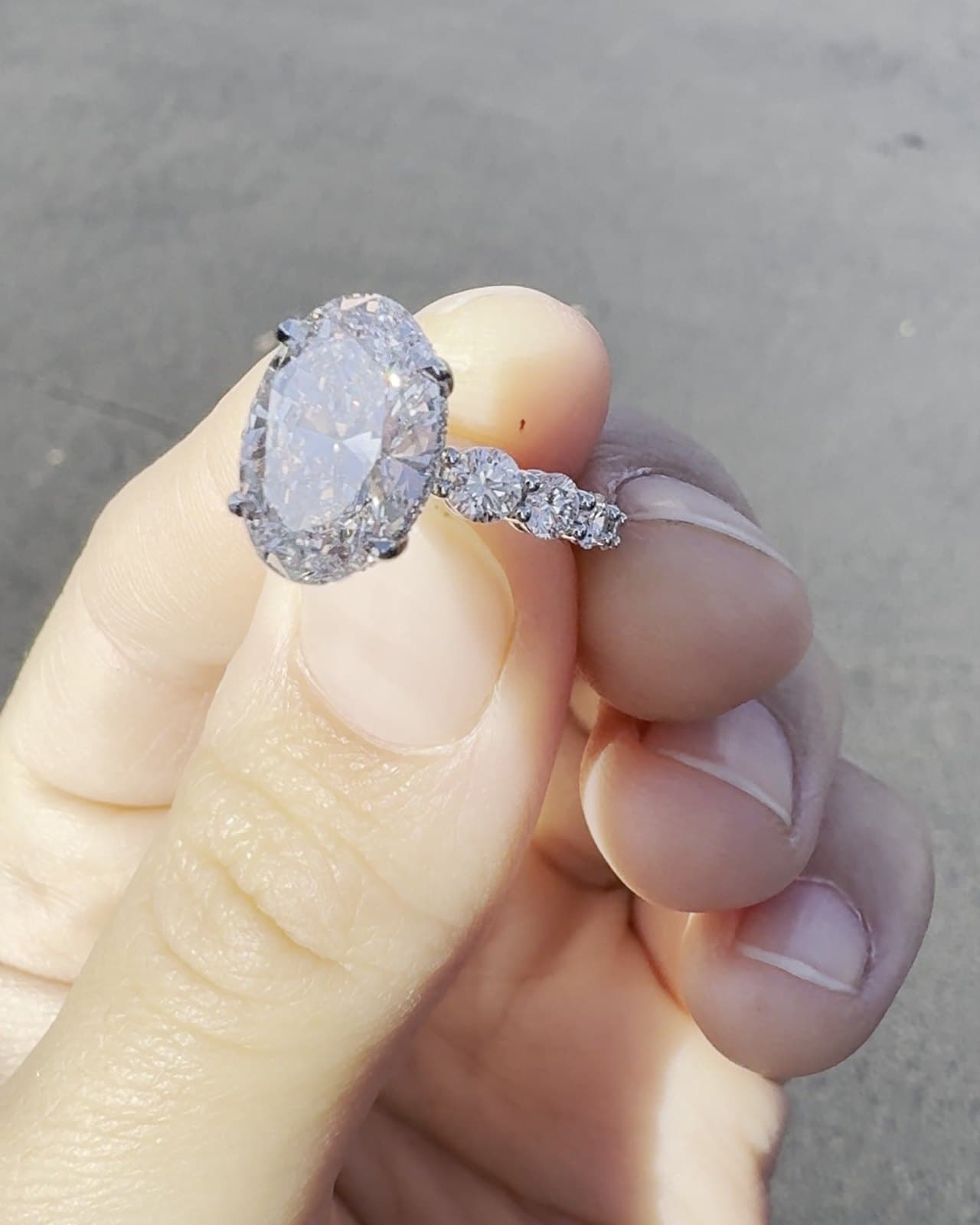 An oval diamond ring with a halo and a band of graduated diamonds, held between two fingers