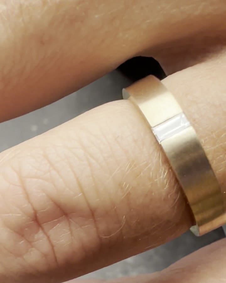A wide gold band with a flush-set baguette diamond, worn on a hand