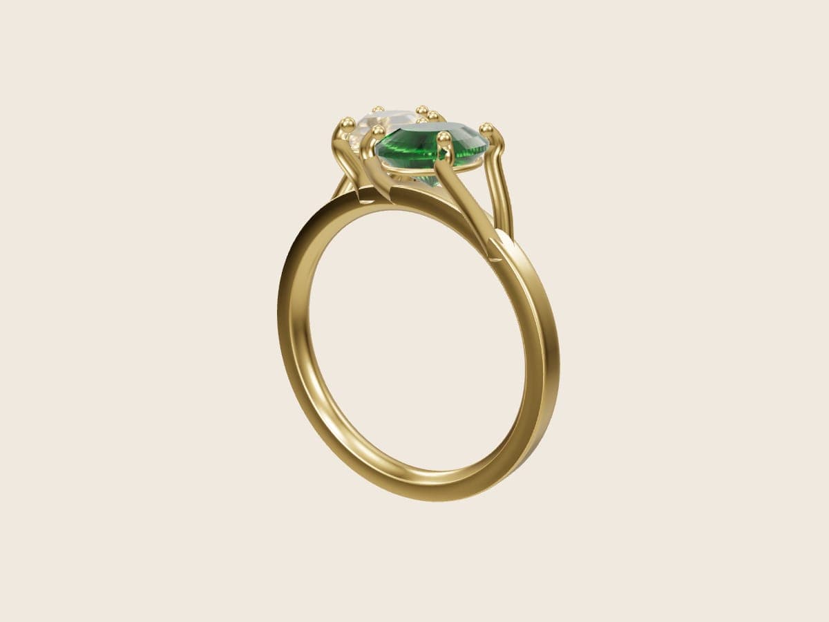 3D render of a toi et moi ring, a pear diamond and an oval emerald set on a diagonal in 14k yellow gold, from the Pacific Jewel Design Studio